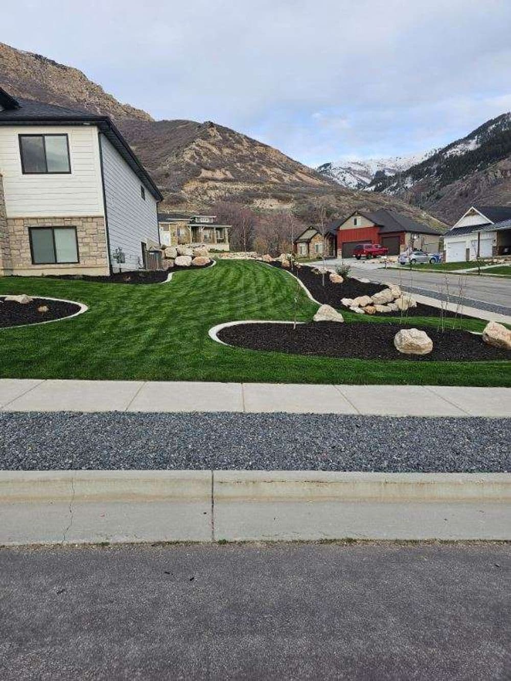 Residential landscape with manicured lawn, decorative rocks, and mountain backdrop.