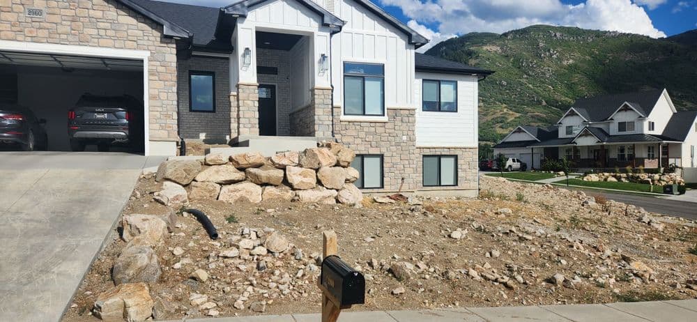 Modern home with stone and siding facade, landscaped yard, and mountain backdrop in residential area.