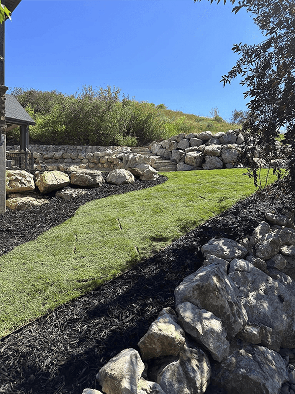 Lush green lawn with decorative stone landscaping under a clear blue sky.