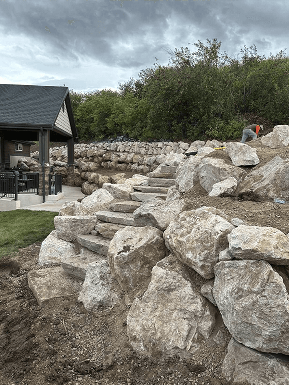 Stone steps leading up a landscaped yard with a house in the background and cloudy skies.