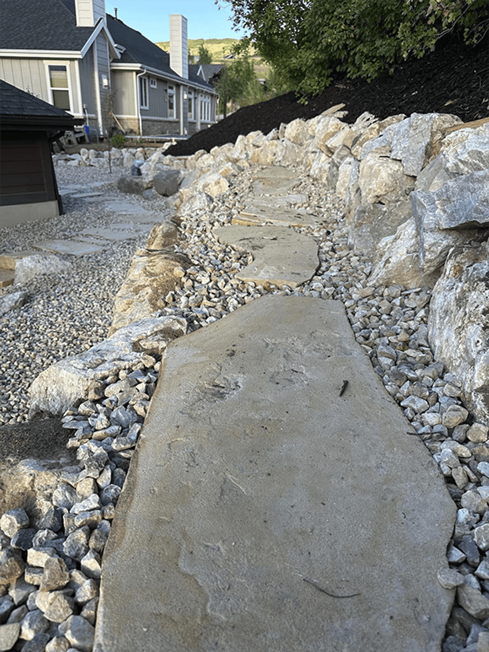 Stone pathway surrounded by pebbles and rocks in a landscaped garden setting.