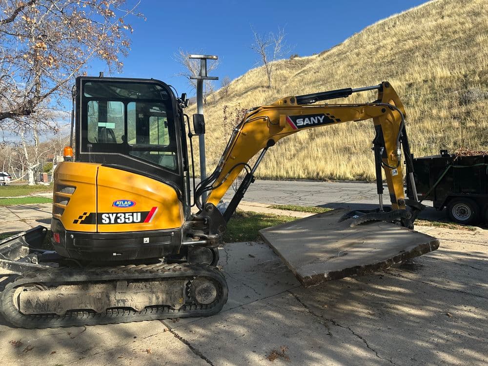 SANY SY35U excavator parked on pavement with grass hillside in background.