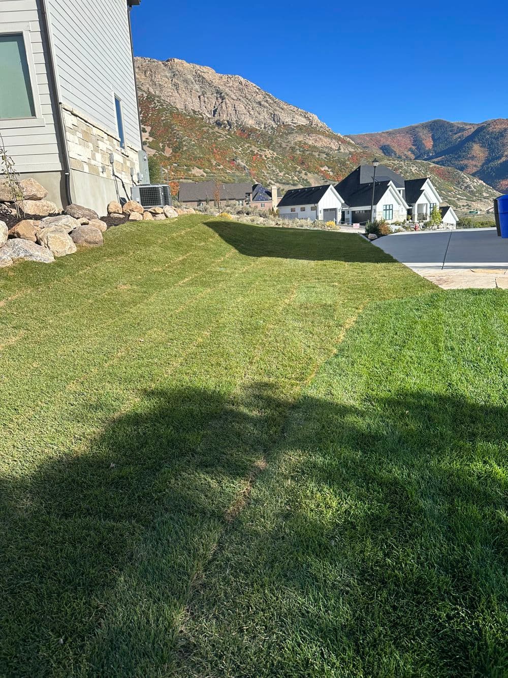 Lawn on a slope with mountains in the background and houses nearby under a clear blue sky.