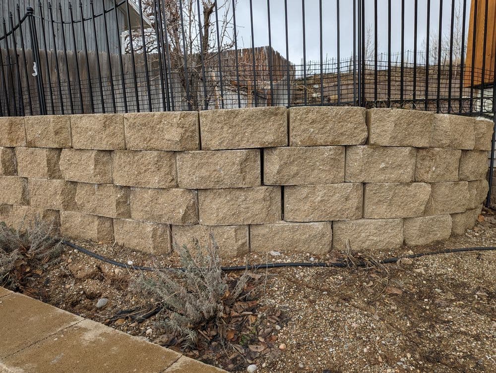 Retaining wall made of large stone blocks, featuring visible cracks and surrounding gravel.