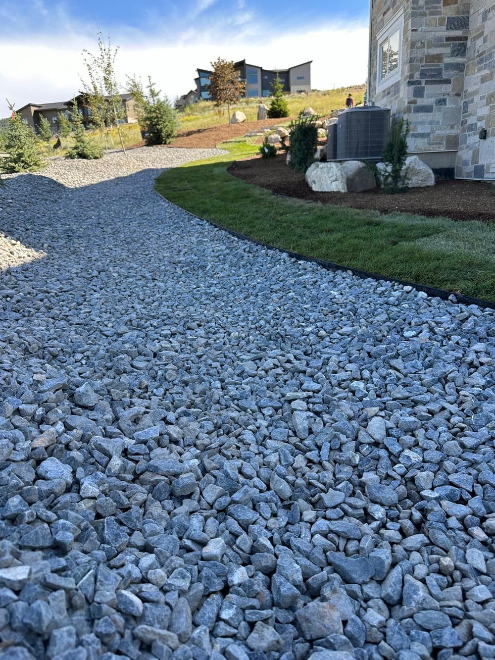 Gravel pathway leading through landscaped yard with homes in the background.